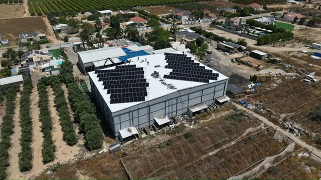 צילום רחפן של מבנה מסחרי עם גג לבן ומערכת סולארית, לצד מטעים