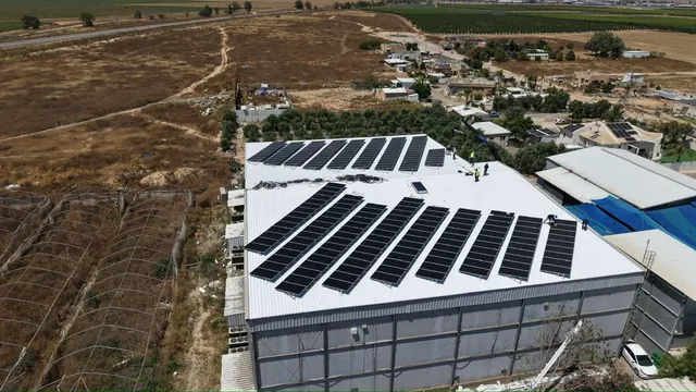 צילום רחפן של מבנה תעשייתי עם גג כחול ומערכת סולארית, ליד שדות חקלאיים