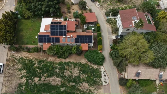 צילום רחפן של וילה בודדת מוקפת ירק עם מערכת סולארית על גג רעפים