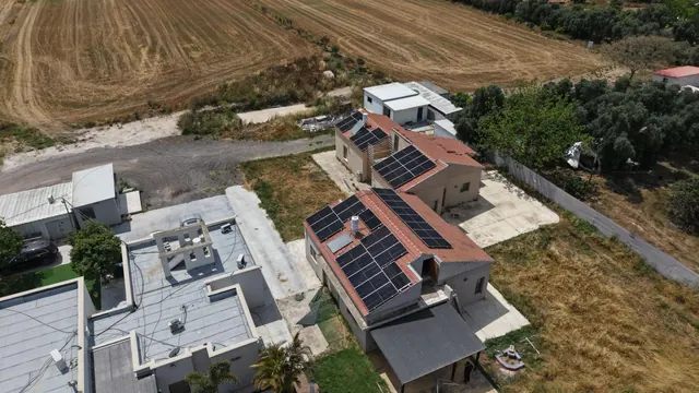 צילום רחפן של בית מודרני עם מערכת סולארית על הגג, מוקף שדות