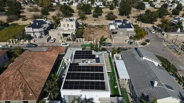 צילום רחפן של בית עם גג רעפים ומערכת סולארית, לצד מבנה מודרני עם גג אפור