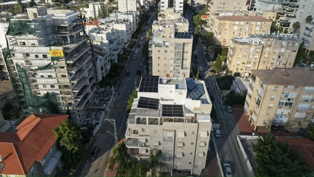 צילום רחפן של גג בניין דירות עירוני עם מערכת סולארית, ברקע בנייני מגורים