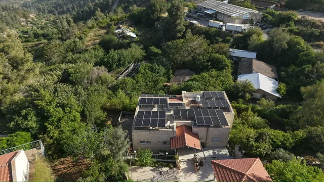 צילום רחפן של וילה מוקפת עצים עם מערכת סולארית על גג רעפים אדום