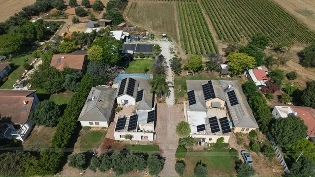 צילום רחפן של כמה מערכות סולאריות על גגות וילות ליד שטח חקלאי